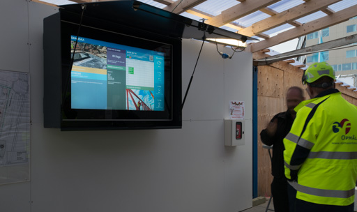 Digital infotavle fra Skanska på byggeplads, der viser leveranceplaner.