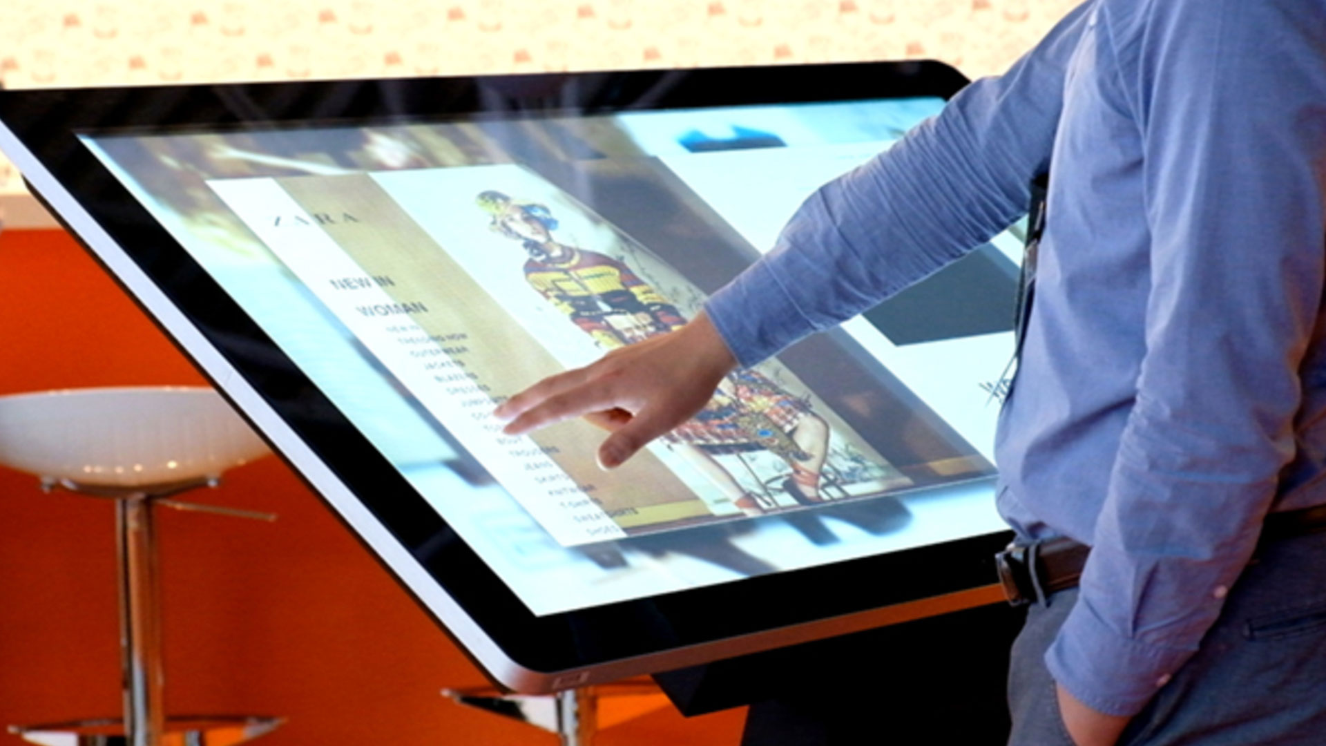 Person bruger touchskærm til at vælge tøj i butik.