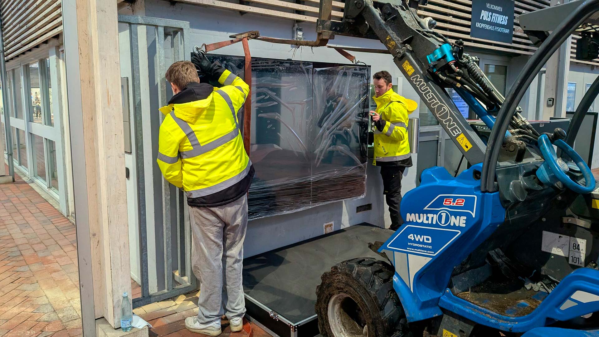 To montører i gul sikkerhedsvest installerer en stor digital skærm i Dianalund.