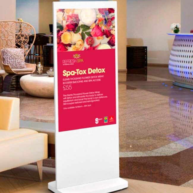 Fritstående hvid poster som viser en reklame for et spaophold, står i lobbyen til et hotel.