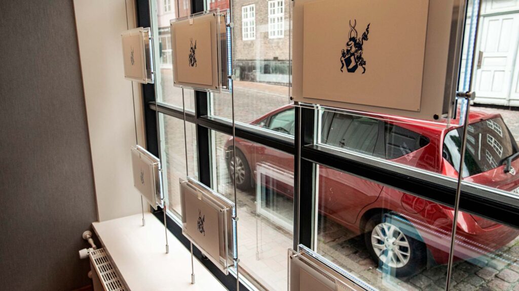 Digitale mæglerskilte til ejendomsmæglere hænger i vinduet hos ejendomsmægler Barfoed Group.