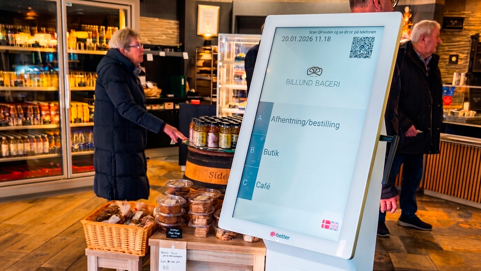 Elektronisk kønummersystem til virksomheder i en bagerbutik med kunder i baggrunden