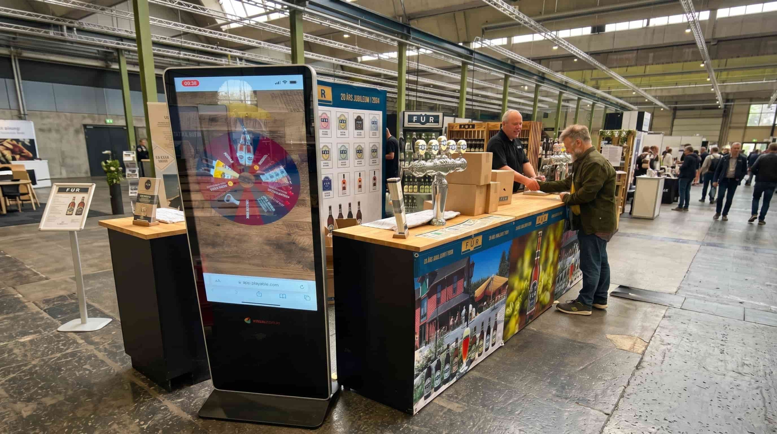 FUR Bryghus mässmonter med fristående skärm (totem) i förgrunden, medan kunder pratar med bryggmästaren i bakgrunden