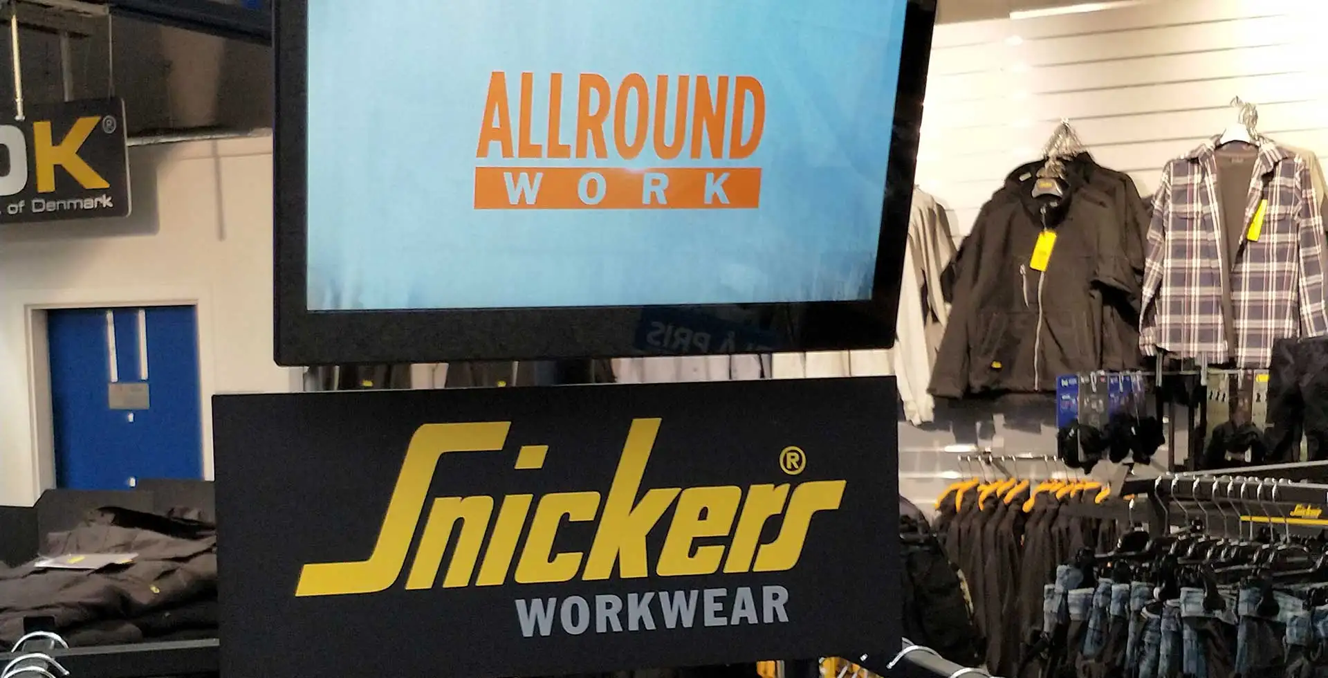 Butiksdisplay på 15 tommer monteret på tøjstativer hos Carl Ras Herlev med oversigt over Snickers Workwear produktlinjer