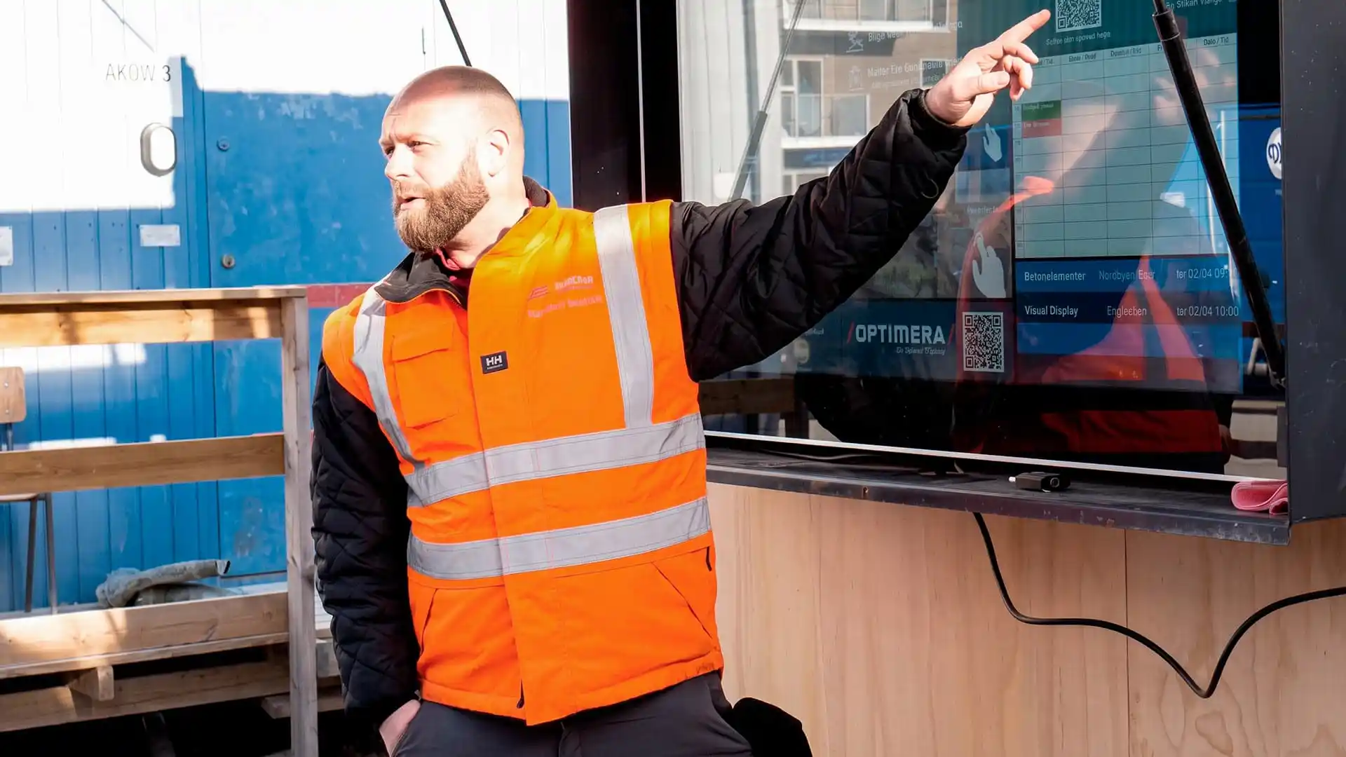 Byggledaren informerar hantverkare vid morgonmöte på digital informationstavla för byggarbetsplatser